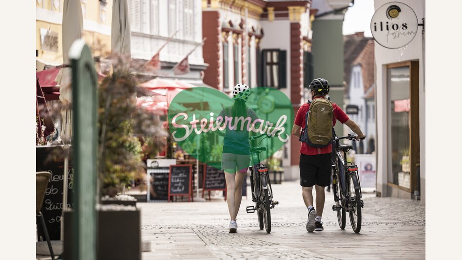 Pärchen spaziert mit Fahrrädern durch die Fußgängerzone von Hartberg | ©  Oststeiermark Tourismus | Velontour