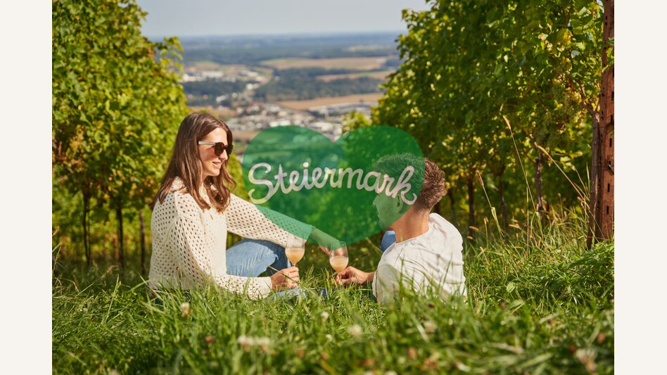 Paar sitzt in der Wiese in einem Weingarten und trinkt Wein in Hartberg in der Oststeiermark | ©  Oststeiermark Tourismus | Markus Lang-Bichl