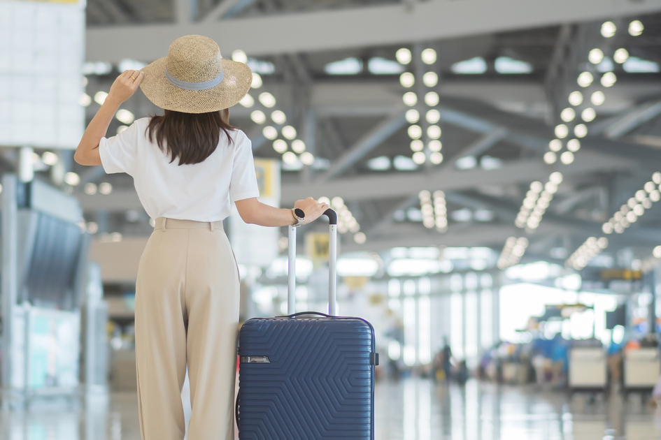 Young woman hand holding luggage handle before checking flight time in airport, Transport, insurance, travel and vacation concepts