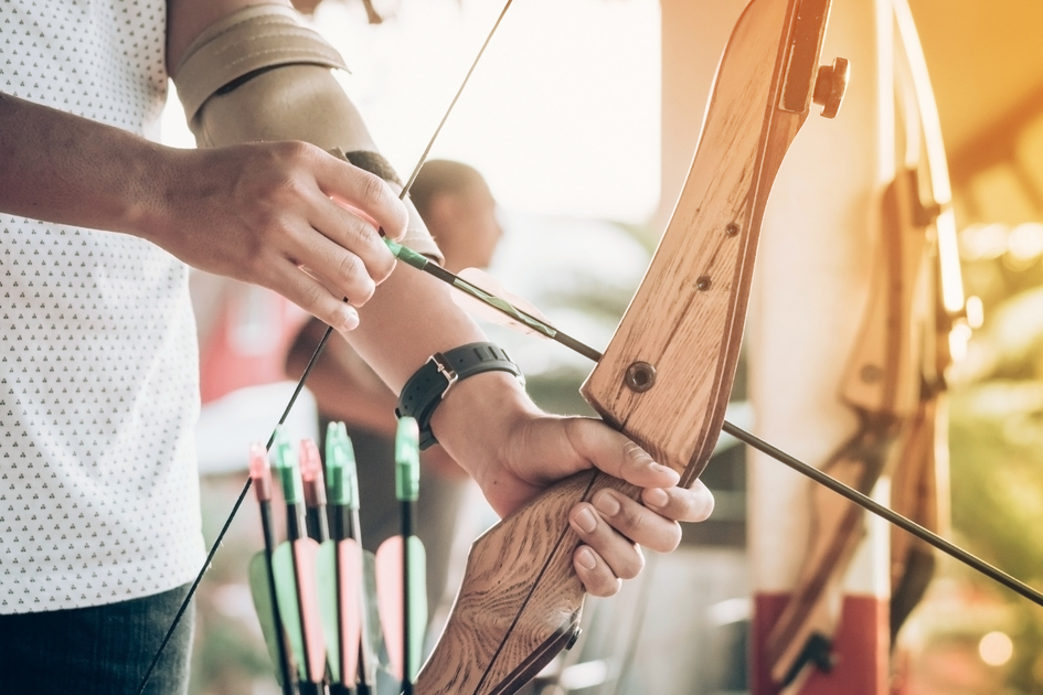 Tourists try to use a bow and arrow and shoot at a target in the amusement park. | © Schilcherland Steiermark | AdobeStock_266956114