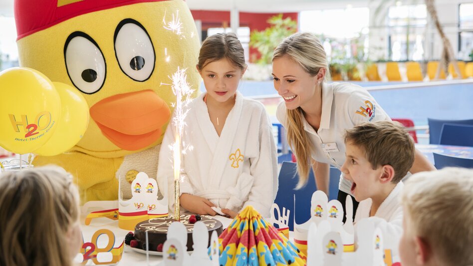 Kind mit Geburtstagstorte dahinter das Thermenmaskottchen