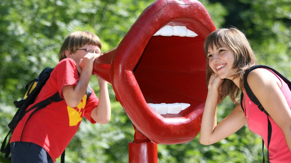 Eine Person lauschend vor einer großen Mund Skulptur
