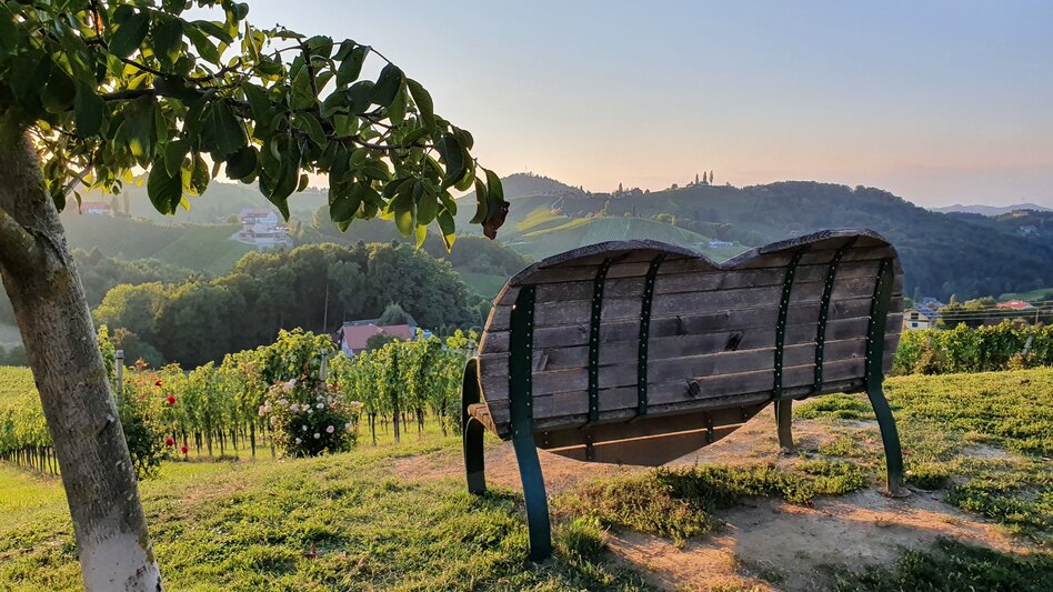 Die Steiermark Herzbank beim Weingut Bullmann an der Südsteirischen Weinstraße: Hier breitet sich die ganze Schönheit des Weinlandes vor einem aus – besonders schön bei Sonnenuntergang. - Günther Steininger | © Steiermark Tourismus | Günther Steininger