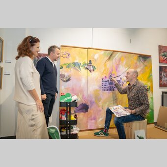 Tom Lohner beim Malen des Expo-Pavillons – Michael Feiertag, GF STG, und Susanne Haubenhofer, GF Erlebnisregion Graz, schauen interessiert zu.  | © STG | Jaden Gynes