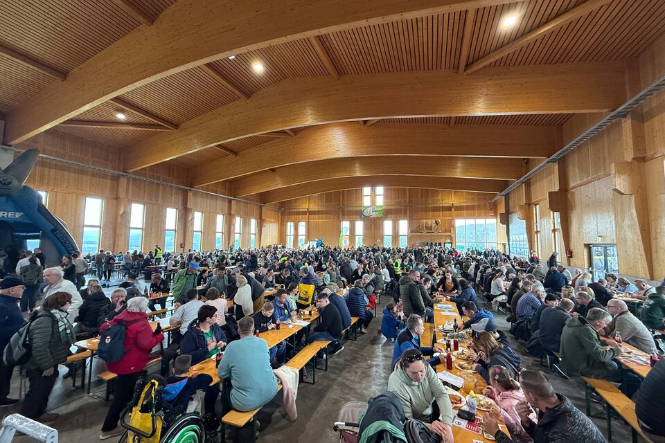 Eine große Menschenmenge in einer gemütlichen Halle mit Holzwänden. Die Gäste sitzen an langen Tischen und genießen ihr Essen. | © SOMA