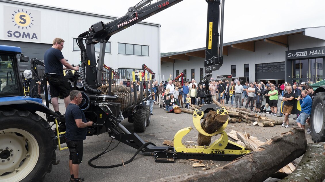 Eine Maschinenvorführung mit einem Traktor und einem Holzgreifer. Viele Zuschauer stehen in der Nähe und beobachten die Aktion. | © SOMA