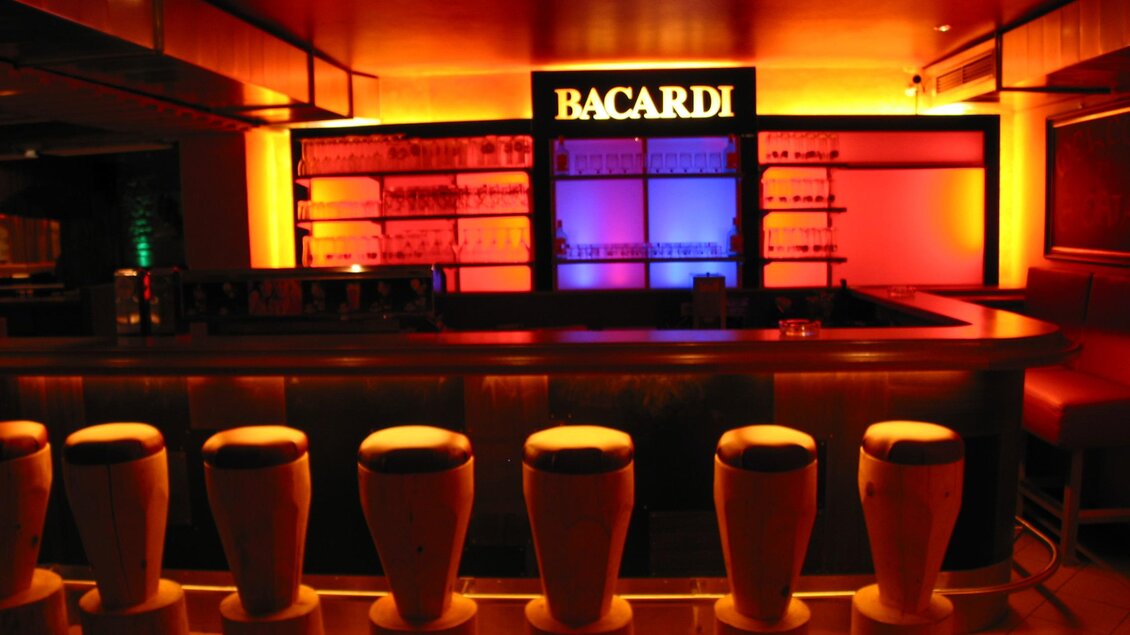 Eine stilvolle Bar mit beleuchteten Regalen und bunten Lichtern. Die Barstühle sind modern und einladend angeordnet. | © Hotel Seebacherhof