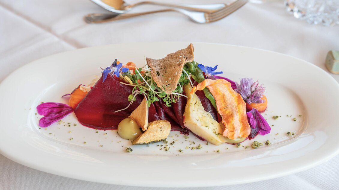 Ein kunstvoll angerichteter Teller mit buntem Gemüse, essbaren Blüten und einer feinen Sauce. Die Präsentation ist elegant und einladend. | © RETTER Bio- Natur- Resort
