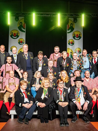 Eine Gruppe von Menschen in traditionellen Kostümen posiert auf einer Bühne. Im Hintergrund sieht man bunte Dekorationen und Scheinwerferlicht. | © Kulturkreis Bad Gleichenberg