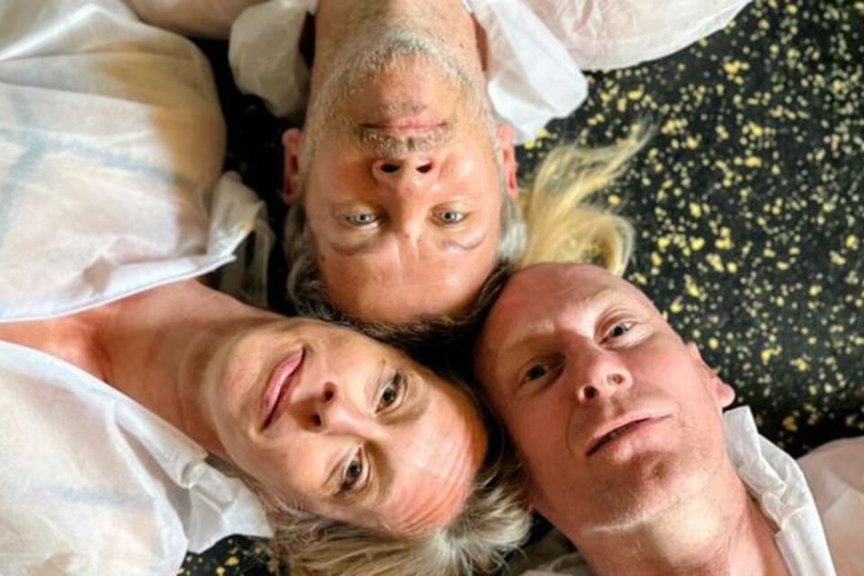 Drei Personen liegen auf dem Boden und schauen zur Kamera. Sie tragen helle Oberbekleidung und der Hintergrund hat ein auffälliges Muster. | © Theaterhaus Graz