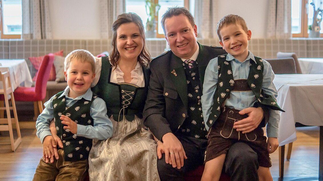 Eine Familie trägt traditionelle bayerische Trachten. Sie lächeln fröhlich in einem gemütlichen Restaurant. | © Naturhotel Bauernhofer