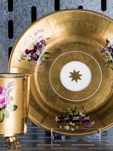 Eine elegante Tasse mit goldener Verzierung und Blumendekoren steht neben einer passenden Untertasse. Beide Teile zeigen kunstvolle Handwerkskunst. | © Markus Mansi_MOMA
