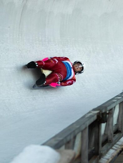 A bobsledder is lying in a tight curve on the racetrack. He is wearing a red suit and is traveling at high speed. | © Pixabay