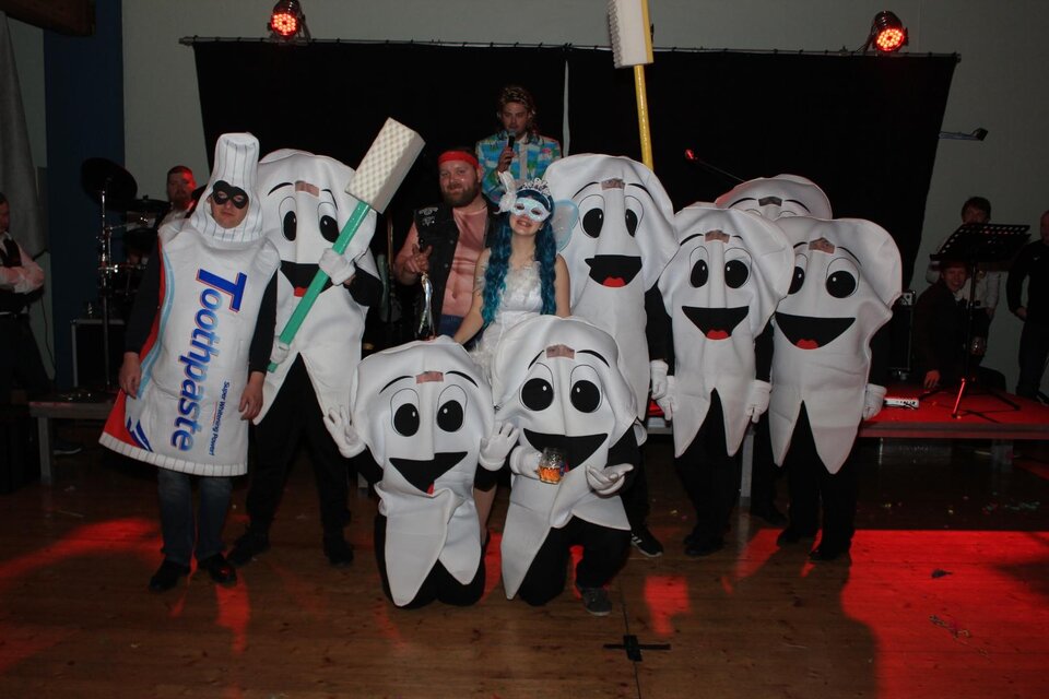Eine Gruppe von Menschen in Zahnmotive-Kostümen, darunter eine Zahnbürste und eine Zahncremetube. Sie posieren fröhlich auf einer Bühne mit Lichtern im Hintergrund. | © Freizeitclub Sebersdorf