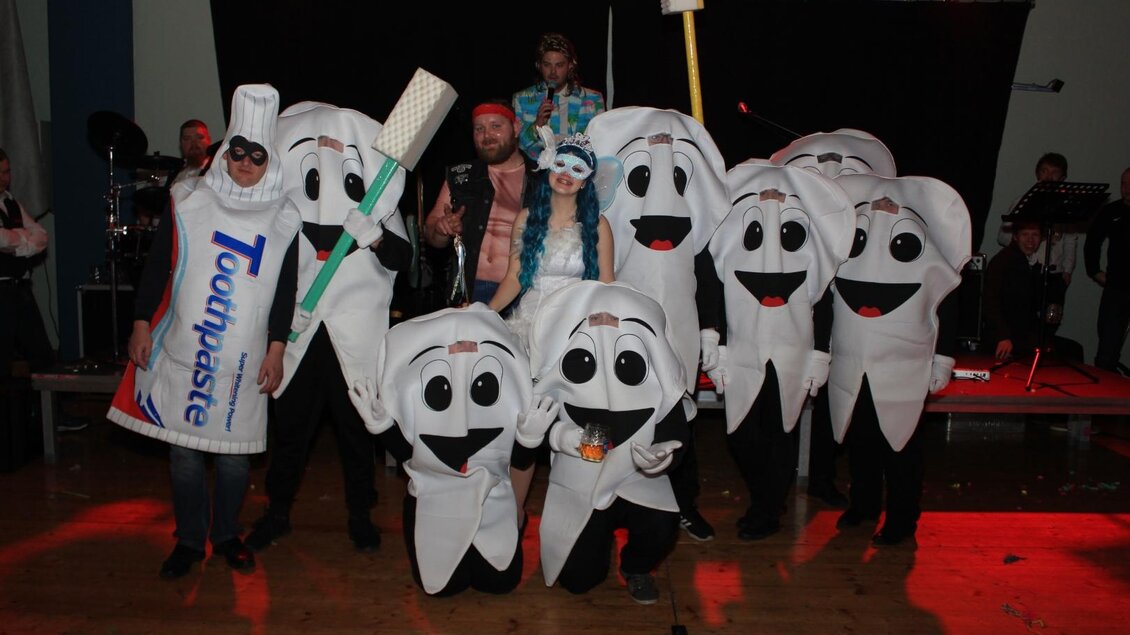 Eine Gruppe von Menschen in Zahnmotive-Kostümen, darunter eine Zahnbürste und eine Zahncremetube. Sie posieren fröhlich auf einer Bühne mit Lichtern im Hintergrund. | © Freizeitclub Sebersdorf