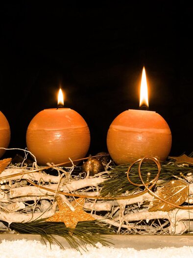 Four burning candles on a decorated tray with branches and fir sprigs. The background is black, creating a festive atmosphere. | © Pixabay