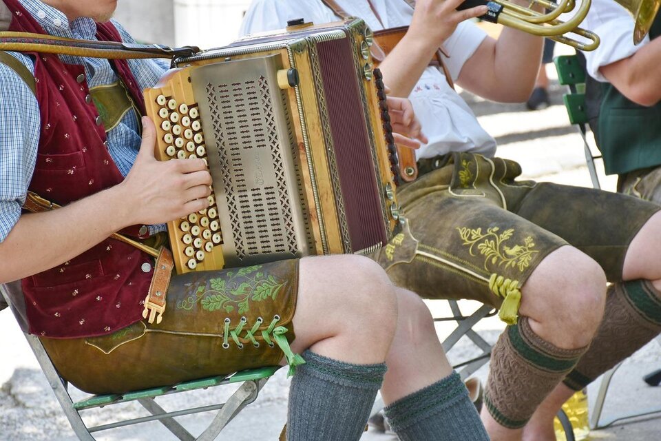 Ein Musiker spielt auf einer Ziehharmonika, während er in Tracht gekleidet ist. Im Hintergrund sind weitere Musiker zu sehen. | © Pixabay