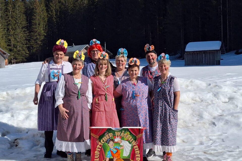 Eine Gruppe von Menschen in traditionellen Trachten steht im Schnee. Im Hintergrund sind Bäume und eine Hütte zu sehen. | ©  Martina Gaisberger