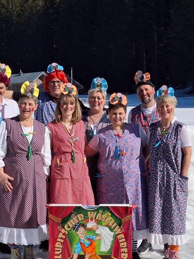 Eine Gruppe von Menschen in traditionellen Deutschen Kleidern steht auf Schnee. Sie lächeln fröhlich und tragen bunte Kopfbedeckungen. | © Martina Gaisberger
