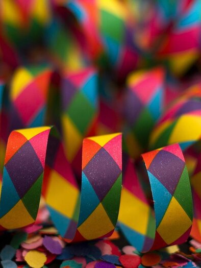 Colorful confetti rolls with a festive pattern. They are lying on a colorful background made of confetti as well. | © pixabay