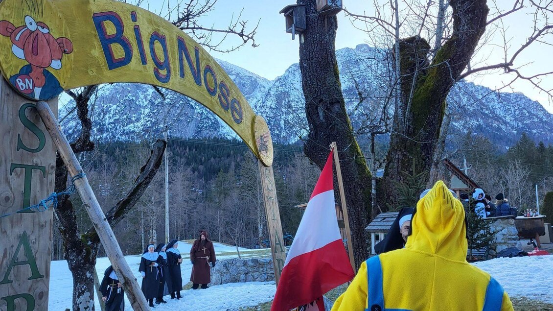 Ein Eingangsschild mit dem Namen "Big Nose" in einer verschneiten Landschaft. Im Hintergrund sind Berge und Menschen in warmer Kleidung zu sehen. | © Petra Kirchschlager
