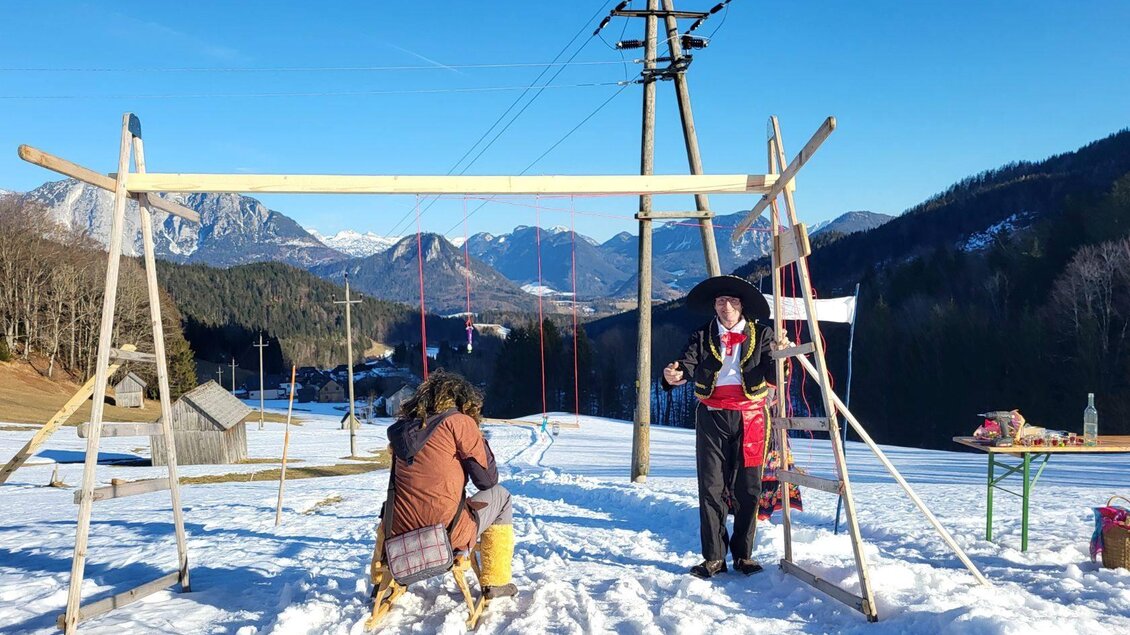 Zwei Personen bauen eine Schaukel aus Holz im Schnee. Im Hintergrund sind Berge und Bäume zu sehen, bei sonnigem Wetter. | © Petra Kirchschlager
