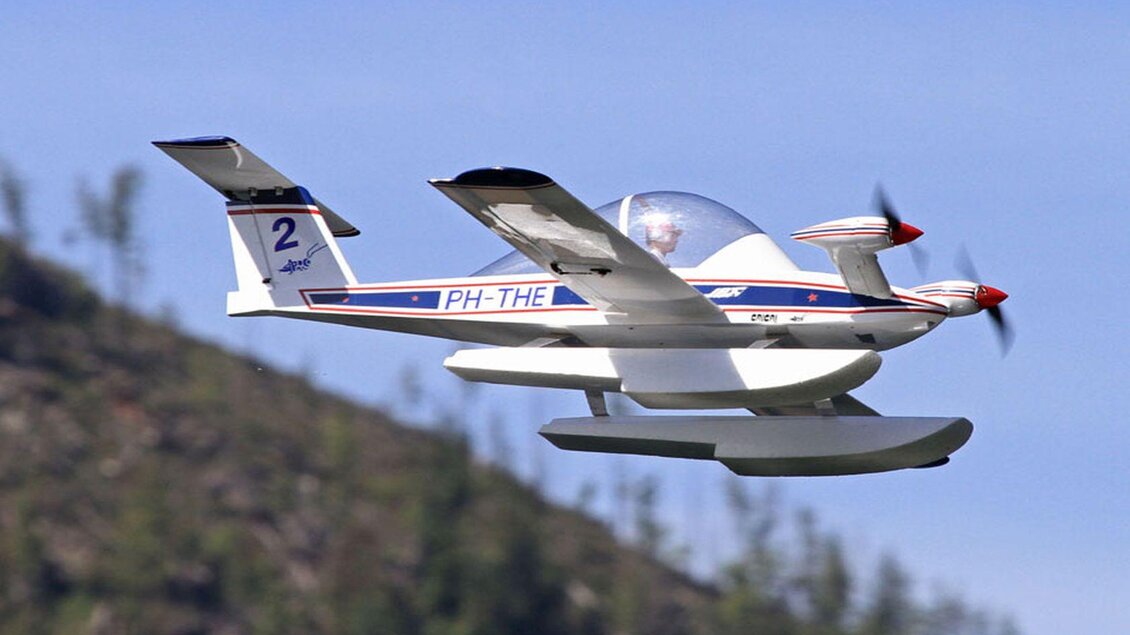 Ein schwimmfähiges Flugzeug fliegt über eine grüne Landschaft. Der Himmel ist klar und blau. | © Ian Walter