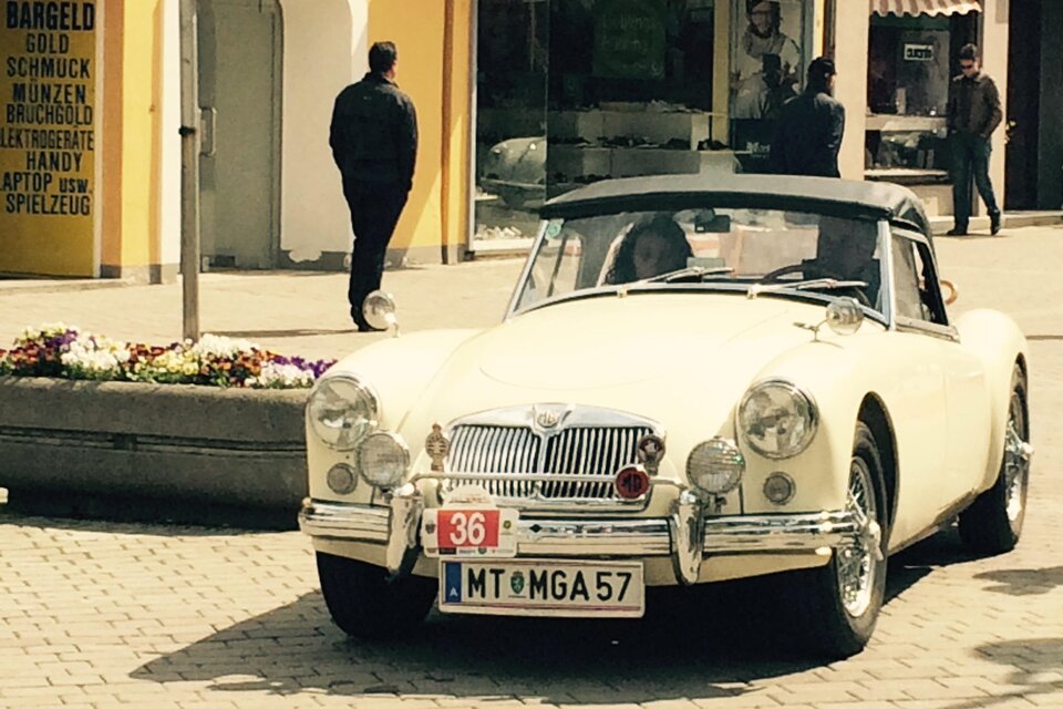 Ein klassisches, weißes Cabriolet parkt auf einer Straßenecke. Im Hintergrund sind Passanten und Geschäfte zu sehen. | © FHF Murtal Classic