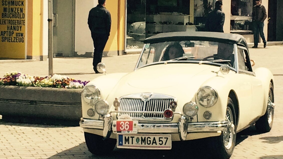 Ein klassisches, weißes Cabriolet parkt auf einer Straßenecke. Im Hintergrund sind Passanten und Geschäfte zu sehen. | © FHF Murtal Classic
