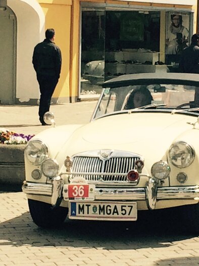 A classic white convertible is parked on a street corner. In the background, passersby and stores can be seen. | © FHF Murtal Classic