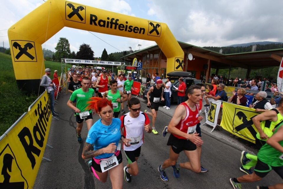Eine Gruppe von Läufern startet einen Wettlauf unter einem auffälligen Startbogen. Die Teilnehmer tragen bunte Sportkleidung und die Stimmung ist enthusiastisch. | © Happy Lauf Anger