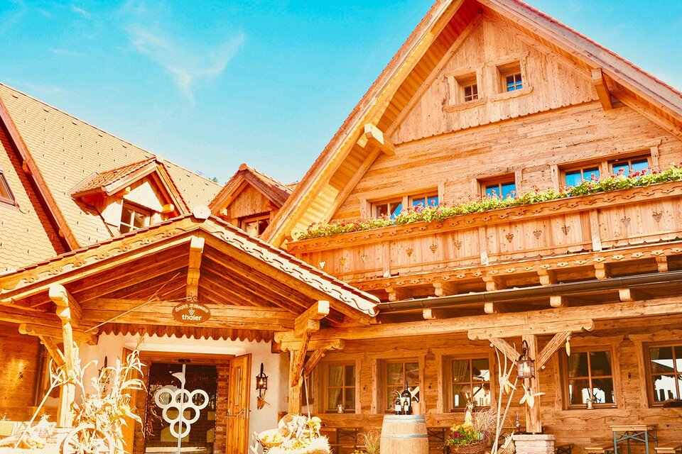 Ein charmantes Holzhaus mit traditioneller Architektur und einem einladenden Eingang. Die Fassade ist hell und gut gepflegt, umgeben von natürlicher Schönheit. | © Buschenschank Fam. Thaler