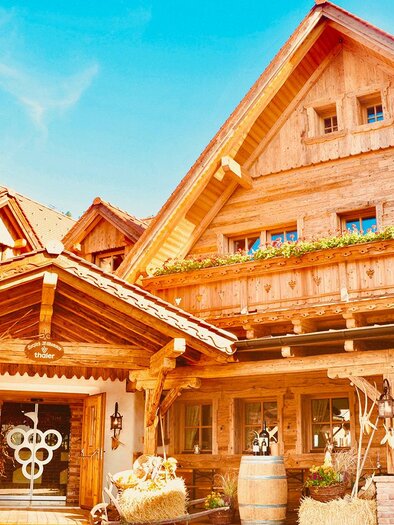 A charming wooden house with traditional architecture and an inviting entrance. The facade is bright and well-maintained, surrounded by natural beauty. | © Buschenschank Fam. Thaler