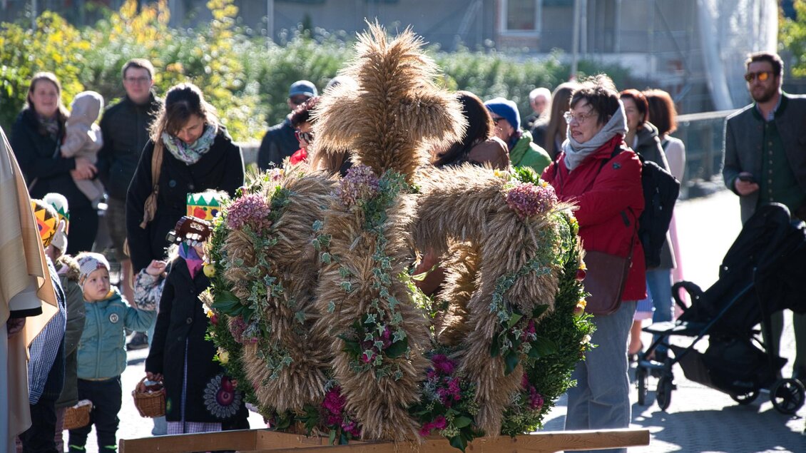 Eine große, strohige Krone ist im Vordergrund zu sehen, umgeben von einer Menschenmenge. Die Veranstaltung findet an einem sonnigen Tag statt und es gibt verschiedene Teilnehmer, die das Fest beobachten. | © Echtzeit TV