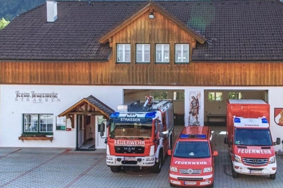 Ein Feuerwehrgebäude mit mehreren Einsatzfahrzeugen. Im Vordergrund stehen zwei rote Feuerwehrwagen und ein weiteres Fahrzeug. | © FF Strassen