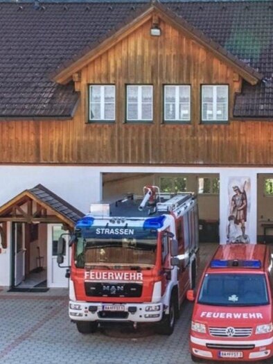 A fire station with several emergency vehicles. In the foreground are two red fire trucks and another vehicle. | © FF Strassen