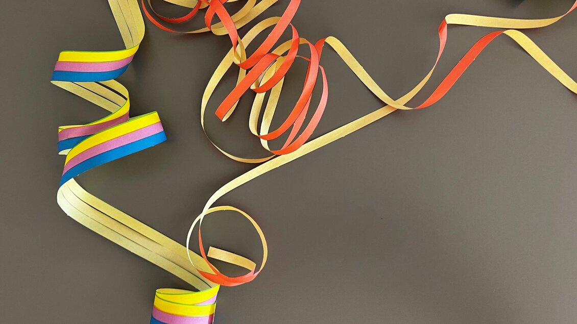 Bunte Geschenkband-Reste liegen chaotisch auf einem dunklen Untergrund. Die Farben umfassen Rot, Gelb, Blau und Grün. | © TV Thermen- & Vulkanland
