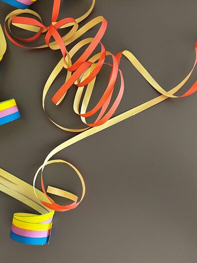 Colorful remnants of gift ribbons lie chaotically on a dark background. The colors include red, yellow, blue, and green. | © TV Thermen- & Vulkanland