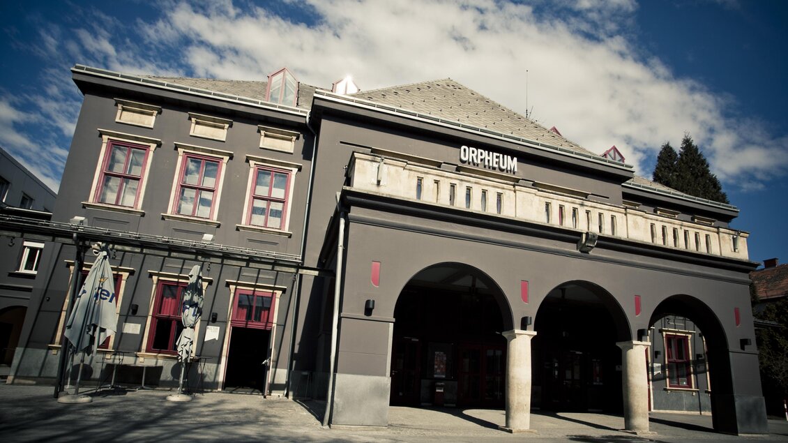 Ein historisches Gebäude mit dem Namen "Orpheum". Es hat einen eleganten Eingang und ist von einem blauen Himmel umgeben. | © (c) Spielstätten - Lupi Spuma