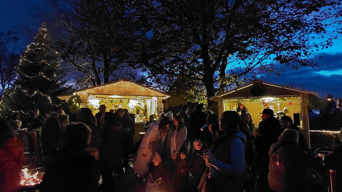 Eine festliche Versammlung bei Nacht mit vielen Menschen und einem Feuer. Im Hintergrund sind geschmückte Hütten und ein Weihnachtsbaum sichtbar. | © Gemeinde Pöllauberg
