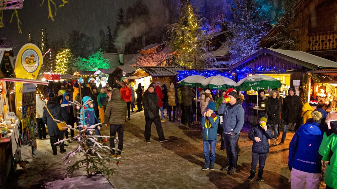 Ein festlicher Weihnachtsmarkt mit vielen Besuchern. Bunte Lichter und Stände mit verteilt Essen sorgen für eine fröhliche Atmosphäre im Schnee. | © TVB Schladming-Dachstein