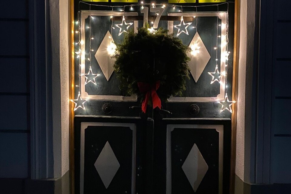 Eine festlich dekorierte Eingangstür mit Lichtern und einem Kranz. Die Tür ist in dunklem Holz gehalten und wird von einem warmen Lichtschein erleuchtet. | © Alexandra Wippel