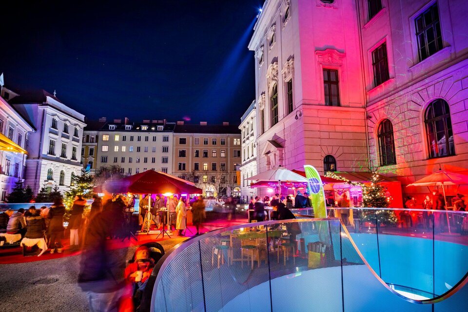Eine lebhafte Nacht mit bunten Lichtern und einer festlichen Atmosphäre. Menschen genießen die Zeit in einem Außenbereich mit verschiedenen Ständen und beleuchteten Gebäuden. | © Graz Tourismus - Werner Krug