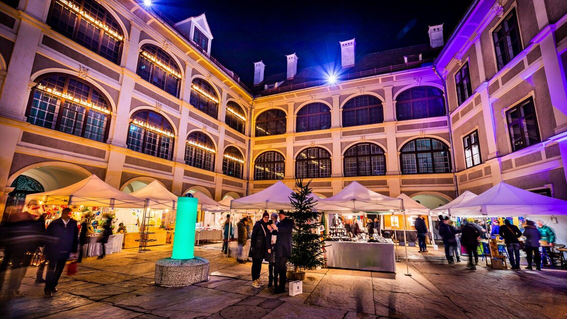 Ein festlich beleuchteter Innenhof mit Marktständen und Besuchern. Die Atmosphäre ist lebhaft und einladend. | © Graz Tourismus - Werner Krug