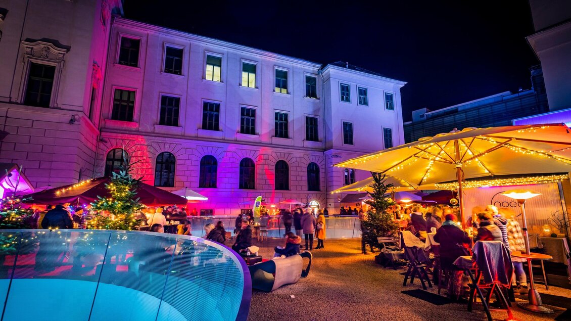 Eine lebendige Abendveranstaltung mit beleuchteten Ständen und Tischen im Freien. Im Hintergrund ist ein historisches Gebäude zu sehen. | © Graz Tourismus - Werner Krug
