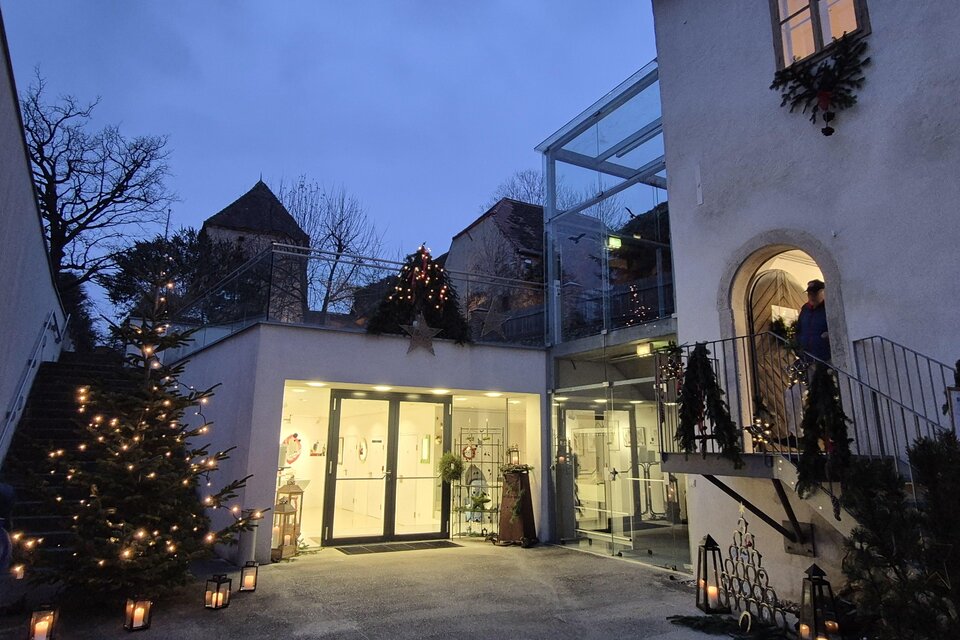 Ein einladender Eingang zu einem Gebäude mit Weihnachtsbeleuchtung und einem Christbaum. Der Himmel ist dämmerig und verleiht der Szenerie eine festliche Atmosphäre. | © Oststeiermark Tourismus