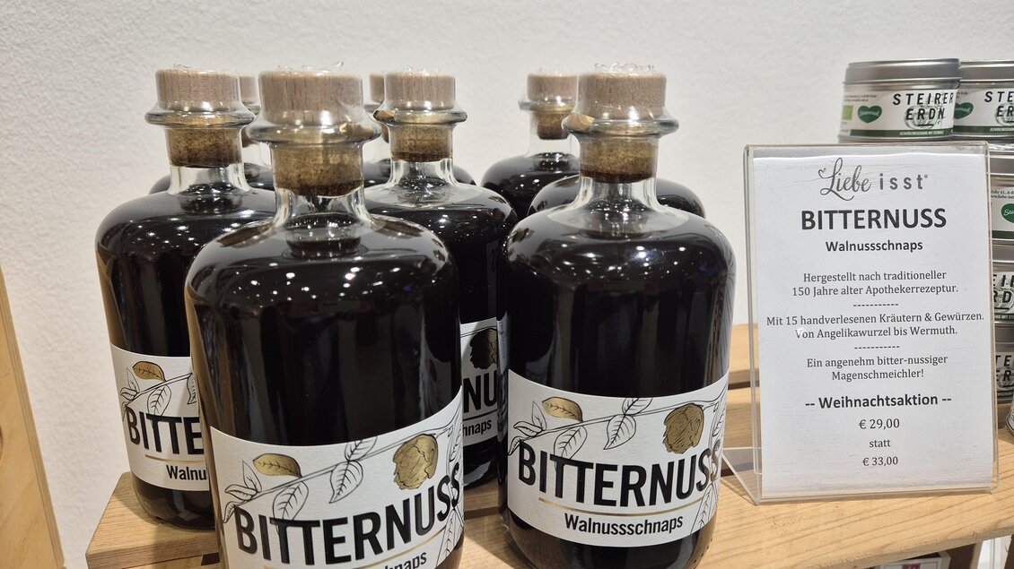 Eine Reihe von Flaschen mit Bitternuss-Walnuss-Schnaps auf einem Regal. Daneben steht ein Preis- und Produktinformationen-Schild. | © Oststeiermark Tourismus