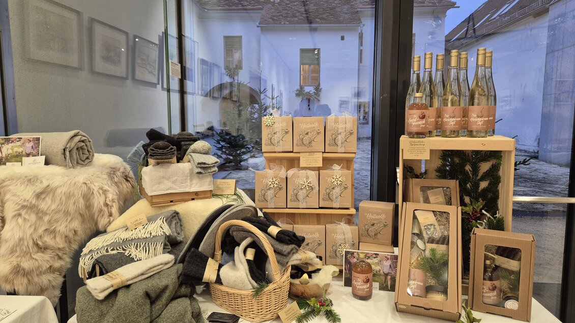 Ein dekorativer Tisch mit verschiedenen Produkten wie Decken, Kerzen und Weinflaschen. Im Hintergrund sieht man einen Innenhof mit einem Fenster. | © Oststeiermark Tourismus