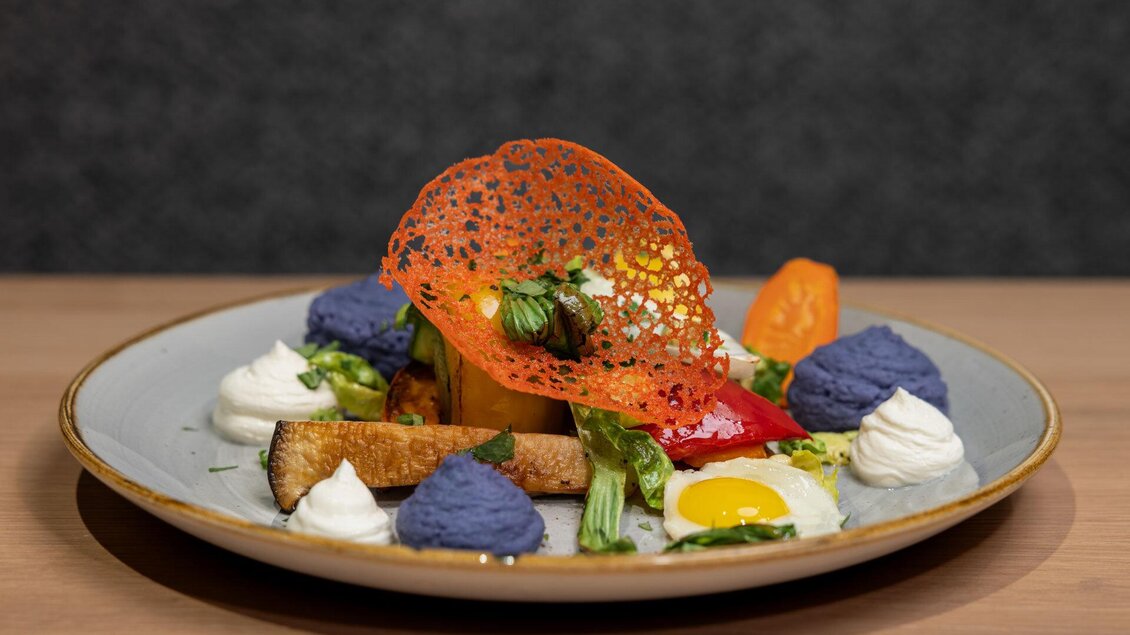 Ein kunstvoll angerichtetes Gericht auf einem Teller, bestehend aus buntem Gemüse, einer Eiklarcreme und einer knusprigen Dekoration. Die Farben sind lebhaft, mit einer schönen Präsentation. | © Martin Huber