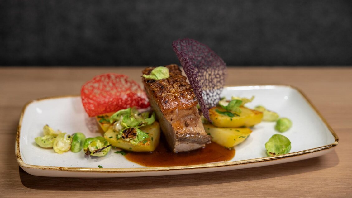 Ein köstliches Gericht mit saftigem Fleisch, buntem Gemüse und einer aromatischen Sauce. Die Präsentation ist kunstvoll mit dekorativen Farbtupfern. | © Martin Huber